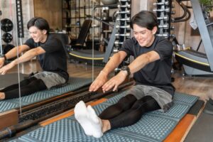 脚を伸ばして座り、前に倒れて太もも裏を伸ばす前屈ストレッチを行う男性