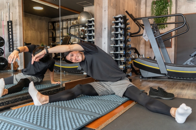 マットに座り、体を横に倒して体側をゆっくり伸ばすストレッチを行う男性